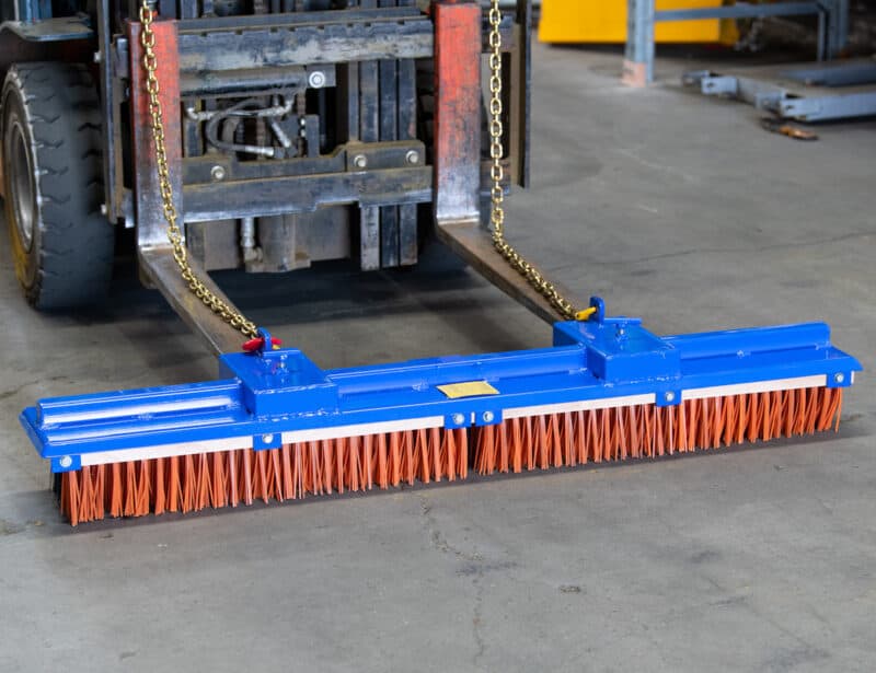 orange and blue broom forklift attachment in a warehouse